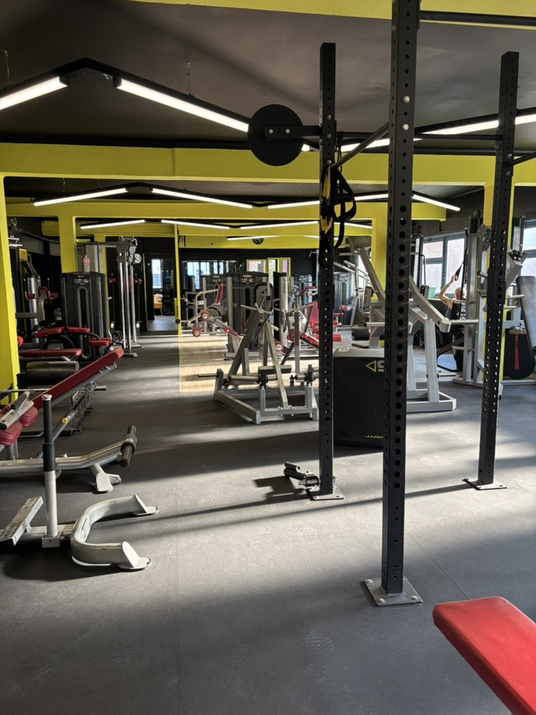Salle de Sport Moderne avec Équipements de Musculation Intérieur d'une salle de sport moderne avec machines de musculation, rack de squat et bancs rouges sous éclairage néon.