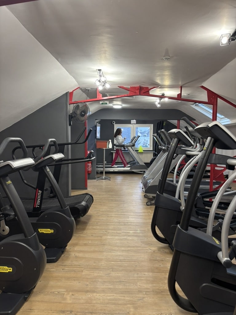 Cardio Technogym : Salle de Sport avec Tapis de Course Tapis de course et vélos elliptiques Technogym dans une salle de sport moderne avec charpente rouge.